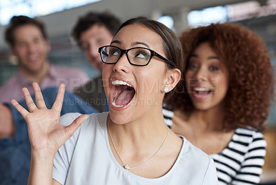 Buy stock photo Young businesswoman shouting and pulling a funny face with colleagues laughing in the background