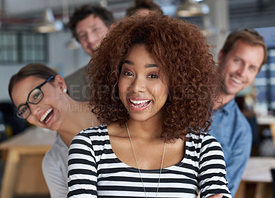 Buy stock photo Closeup portrait of a smiling young woman with friendly coworkers peeping out behind her