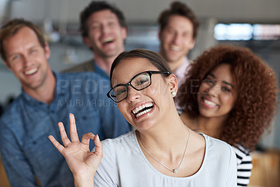 Buy stock photo Young woman smiling cheekily at the camera with colleagues in the background