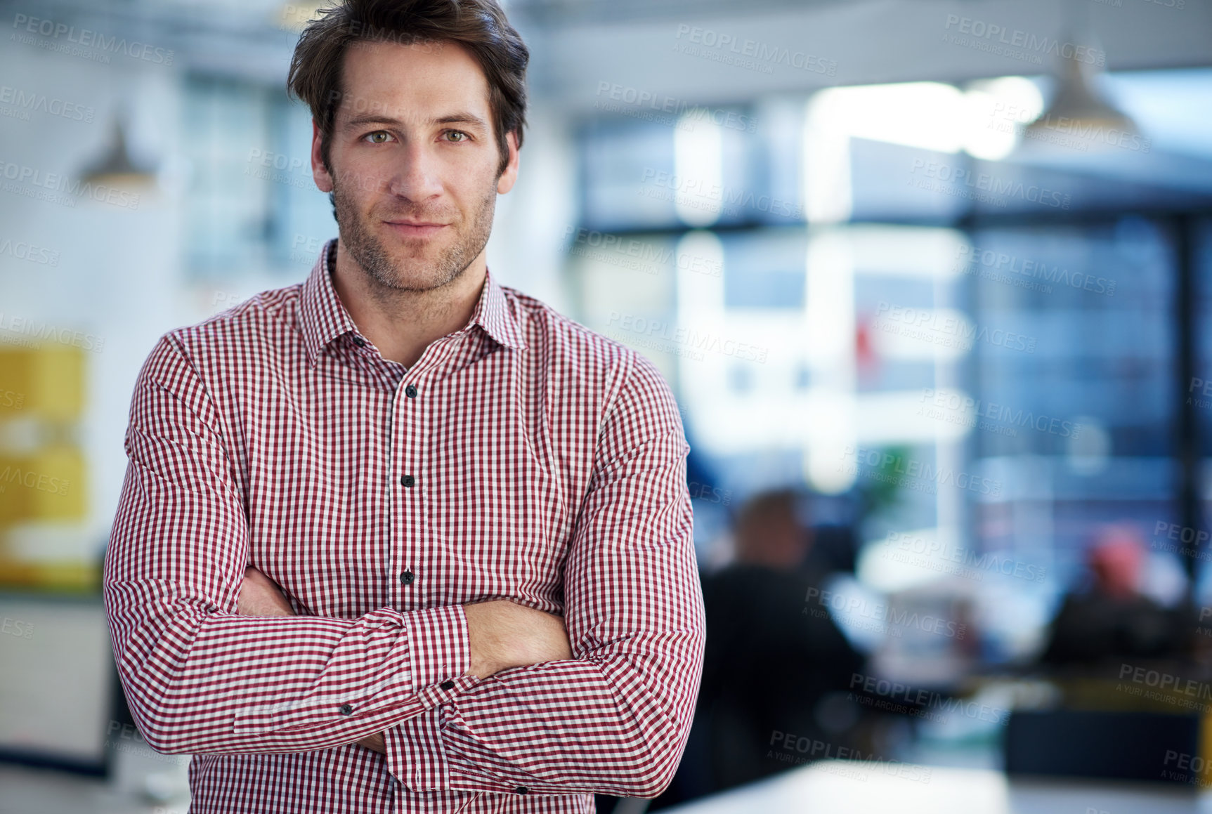 Buy stock photo Cropped shot of a handsome man looking seriously at the camera with open office space behind him
