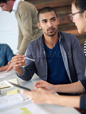Buy stock photo Shot of two coworkers sitting at a table in an office using a digital tablet