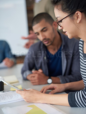 Buy stock photo Shot of two coworkers sitting at a table in an office using a digital tablet