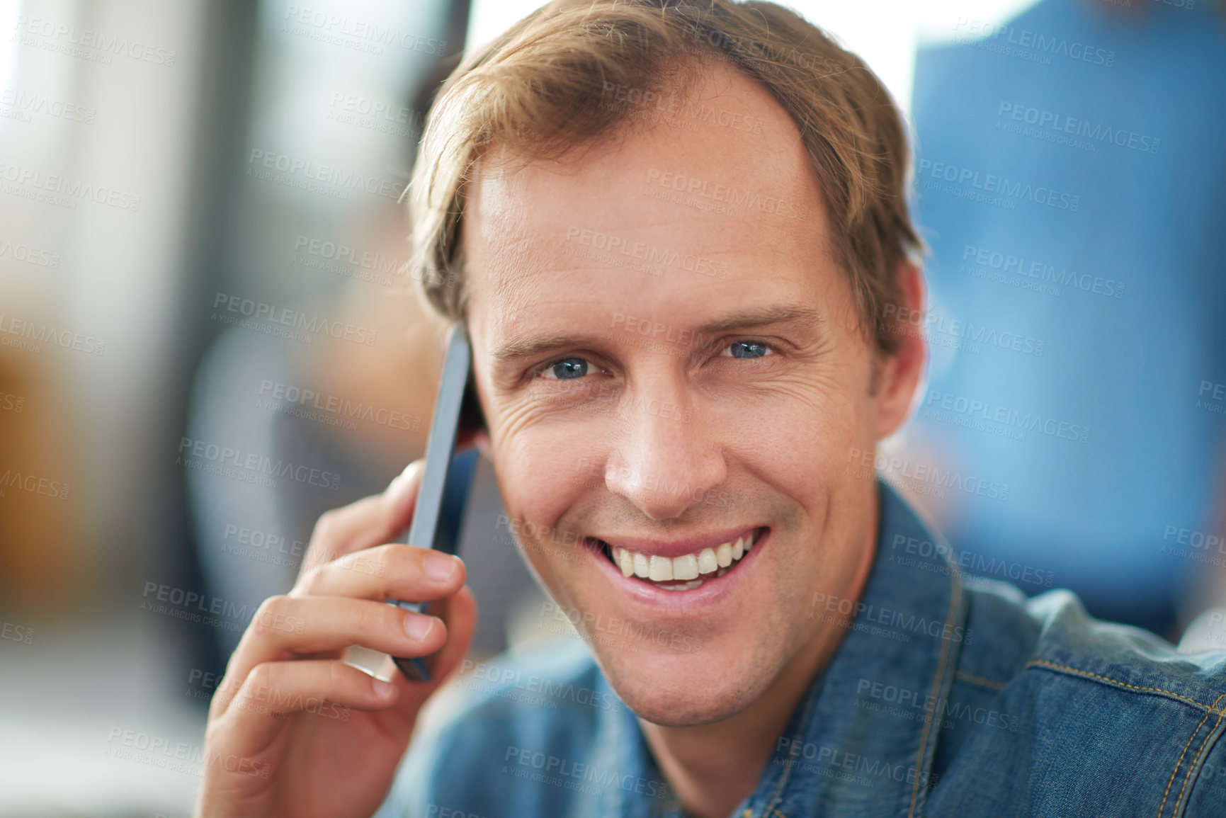 Buy stock photo Shot of a man sitting in an office talking on a cellphone with colleagues in the background