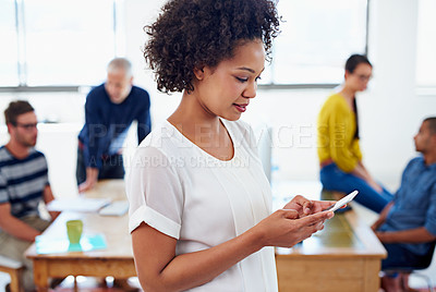 Buy stock photo Beautiful young businesswoman texting on her phone with her office and staff in the background