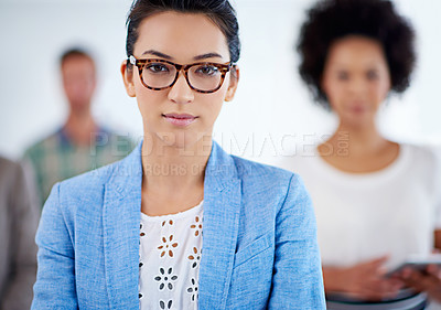 Buy stock photo Cropped portrait of a serious young businesswoman with colleagues in the background