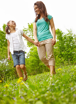 Buy stock photo A mother and daughter holding hands and looking at each other lovingly while walking in a meadow