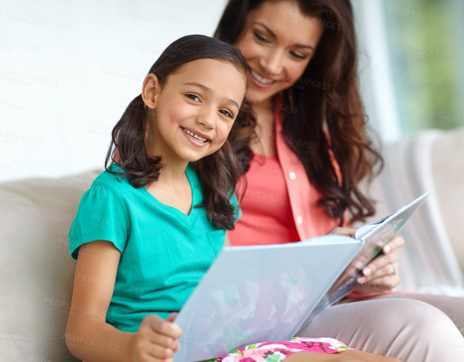 Buy stock photo A pretty girl smiling at the camera while reading a book with her mother