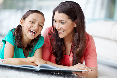 Buy stock photo A laughing mother and daughter lying on the floor with a magazine infront of them sharing a moment