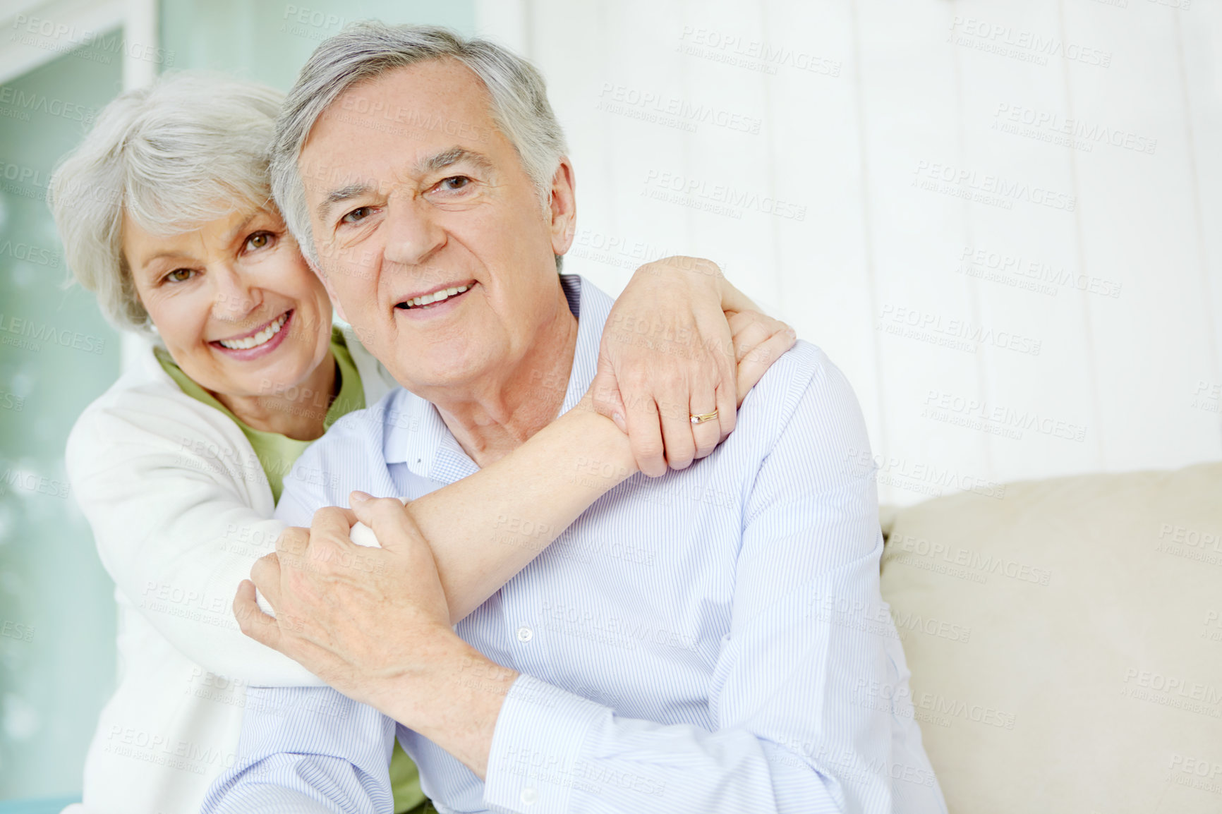 Buy stock photo Hug, portrait and trust with old couple on sofa in home living room together for bonding or commitment. Face, love or smile of senior man and woman embracing in apartment for retirement or security