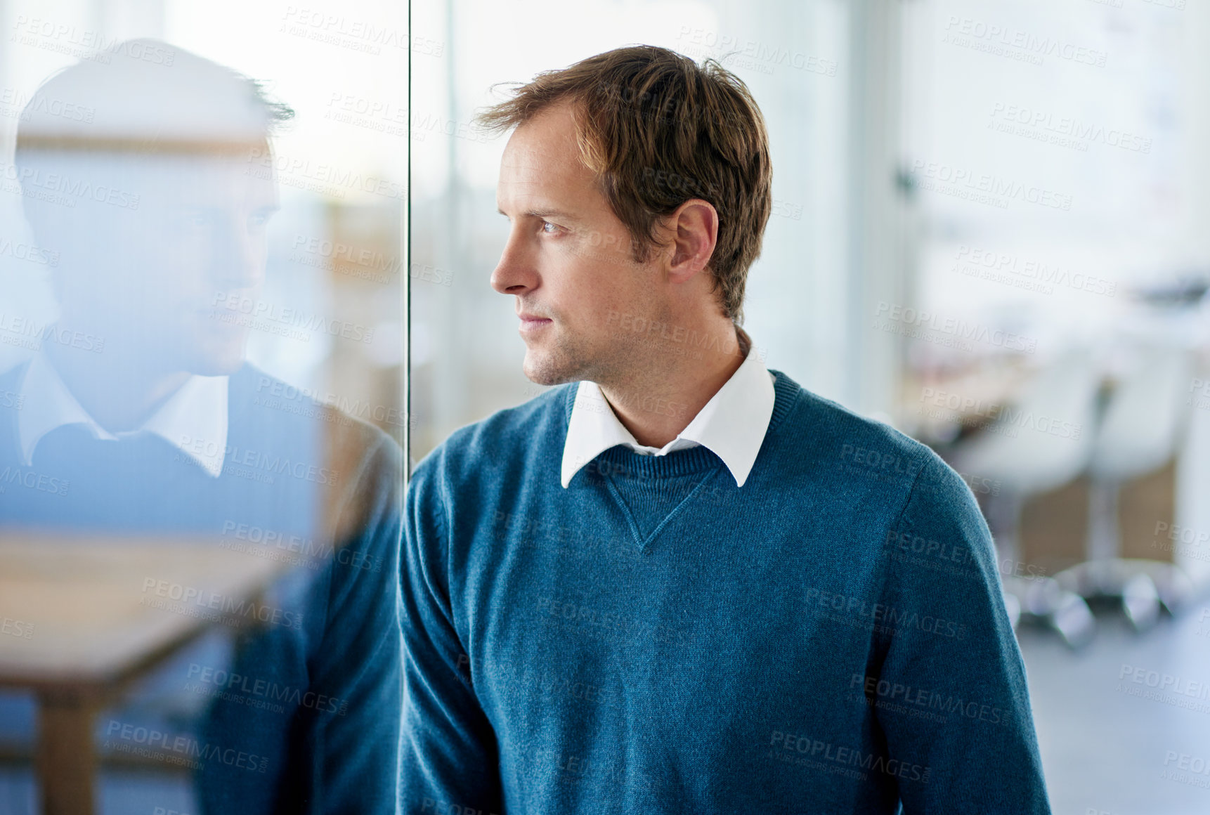 Buy stock photo Shot of a handsome businessman looking through a glass window in an office