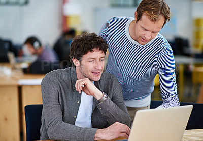 Buy stock photo Shot of two coworkers working together on a laptop in a casual work environment