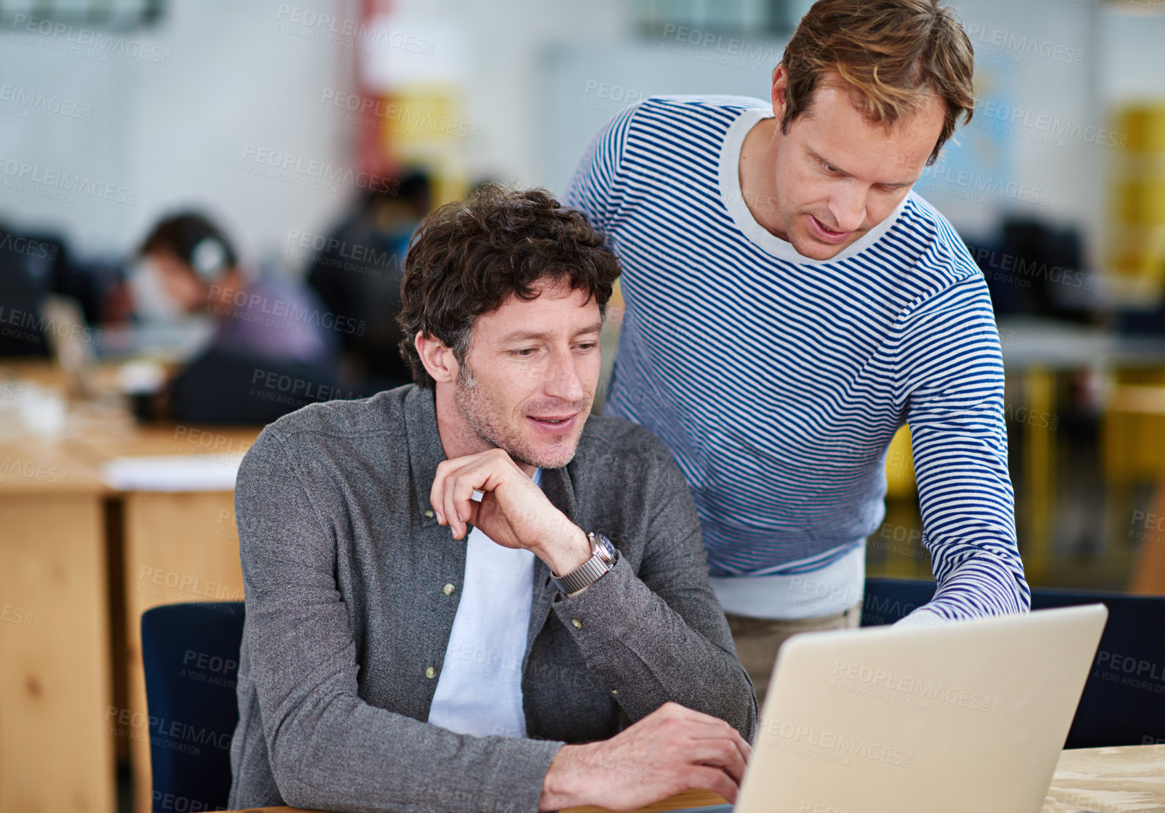 Buy stock photo Shot of two coworkers working together on a laptop in a casual work environment