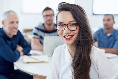 Buy stock photo Portrait of a young office worker sitting at a table with colleagues in the background