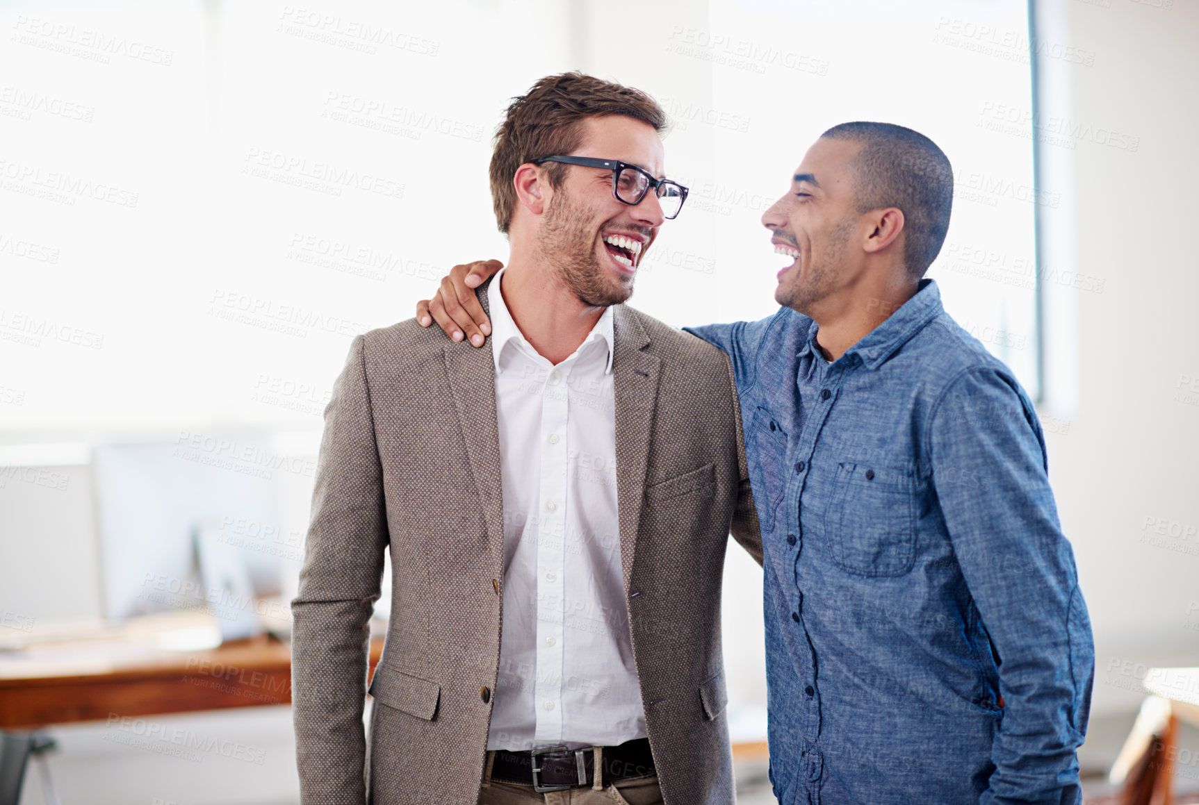 Buy stock photo Shot of two colleagues standing arm in arm in an office