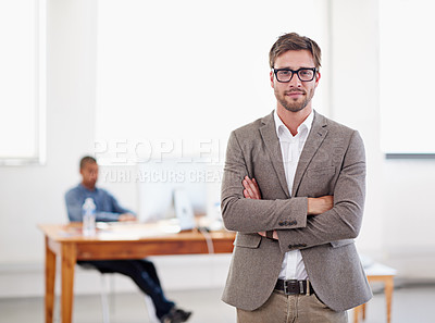 Buy stock photo Portrait of a young man standing in an office with a coworker in the background