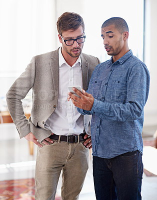 Buy stock photo Shot of two coworkers standing in an office looking at a digital tablet