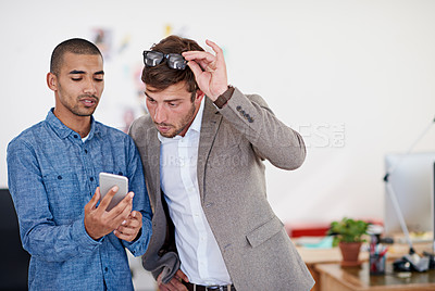 Buy stock photo Shot of two coworkers standing in an office looking at a digital tablet