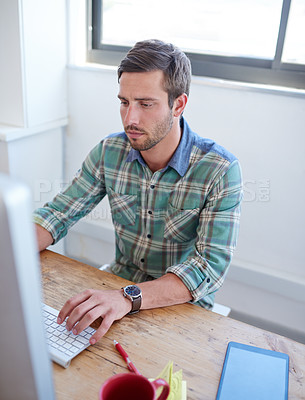 Buy stock photo Cropped shot of a handsome young man working on his pc in the office