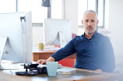 Buy stock photo Mature man looking seriously at the camera while sitting at his desk in an open plan office