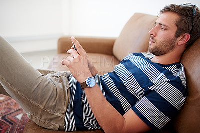 Buy stock photo Young man slouching on a couch using his smart phone