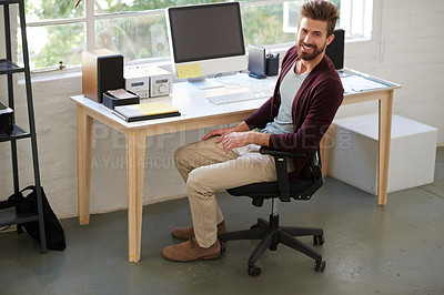 Buy stock photo High angle shot of a young creative professional drinking coffee at his desk and smiling at the camera