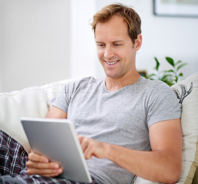 Buy stock photo Shot of a handsome man relaxing with his tablet at home