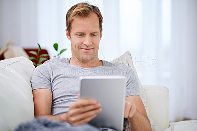 Buy stock photo Shot of a handsome man relaxing with his tablet at home