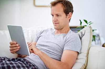 Buy stock photo Shot of a handsome man using his digital tablet at home