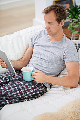 Buy stock photo Shot of a handsome man having coffee while using his tablet at home