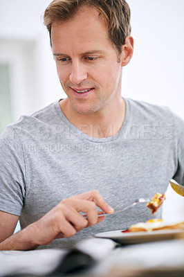 Buy stock photo Shot of a handsome man reading the paper while eating breakfast