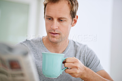 Buy stock photo Shot of a handsome man reading the paper while drinking  coffee at home