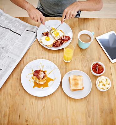 Buy stock photo High angle shot of a man eating breakfast while reading the morning paper