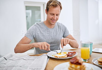 Buy stock photo Shot of a handsome man eating breakfast while reading the morning paper