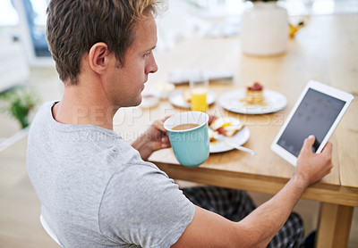 Buy stock photo Shot of a handsome man using his tablet while having breakfast at home