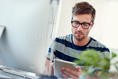 Buy stock photo Shot of a casually-dressed young man using a digital tablet at his desk