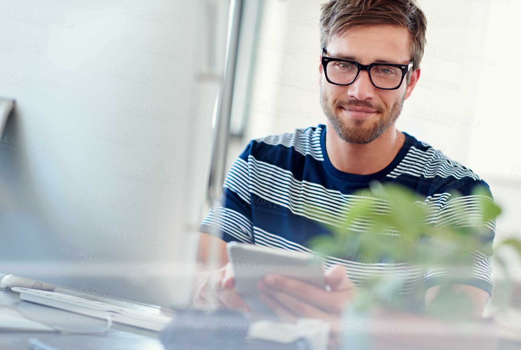 Buy stock photo Portrait of a casually-dressed young man using a digital tablet at his desk