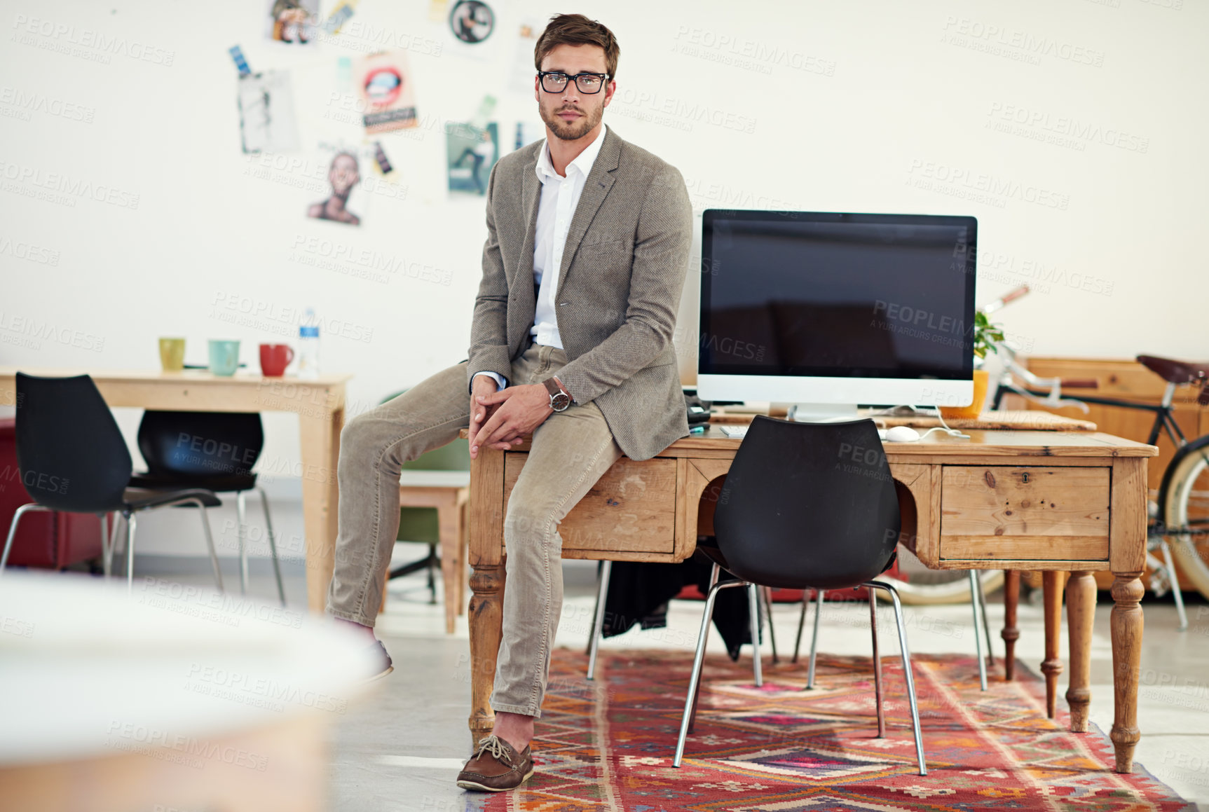 Buy stock photo Portrait of a casually-dressed young man sitting on his desk in an office