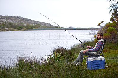 Buy stock photo Shot of a handsome young man fishing by a lake