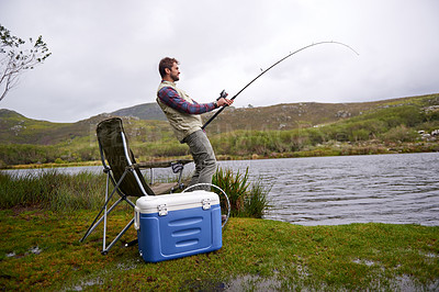 Buy stock photo Shot of a handsome young man fishing by a lake