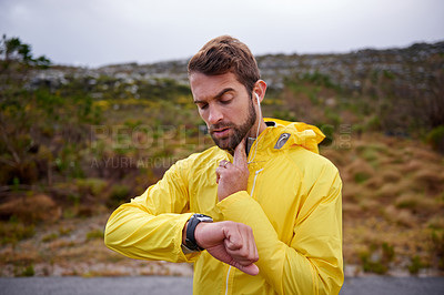 Buy stock photo Shot of a handsome young man checking his heart rate while running in rainy weather