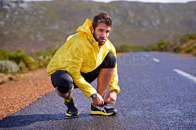 Buy stock photo Shot of a handsome young man tie-ing his shoelace on a rural