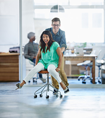 Buy stock photo Shot of a male coworker pushing his female coworker around an office in a chair