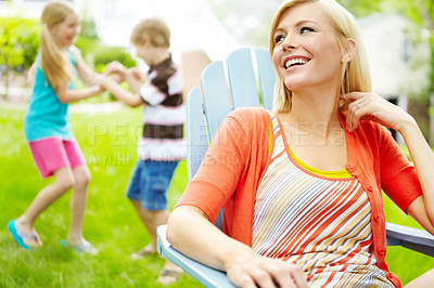 Buy stock photo Happy young mother sitting outdoors as her children play behind her