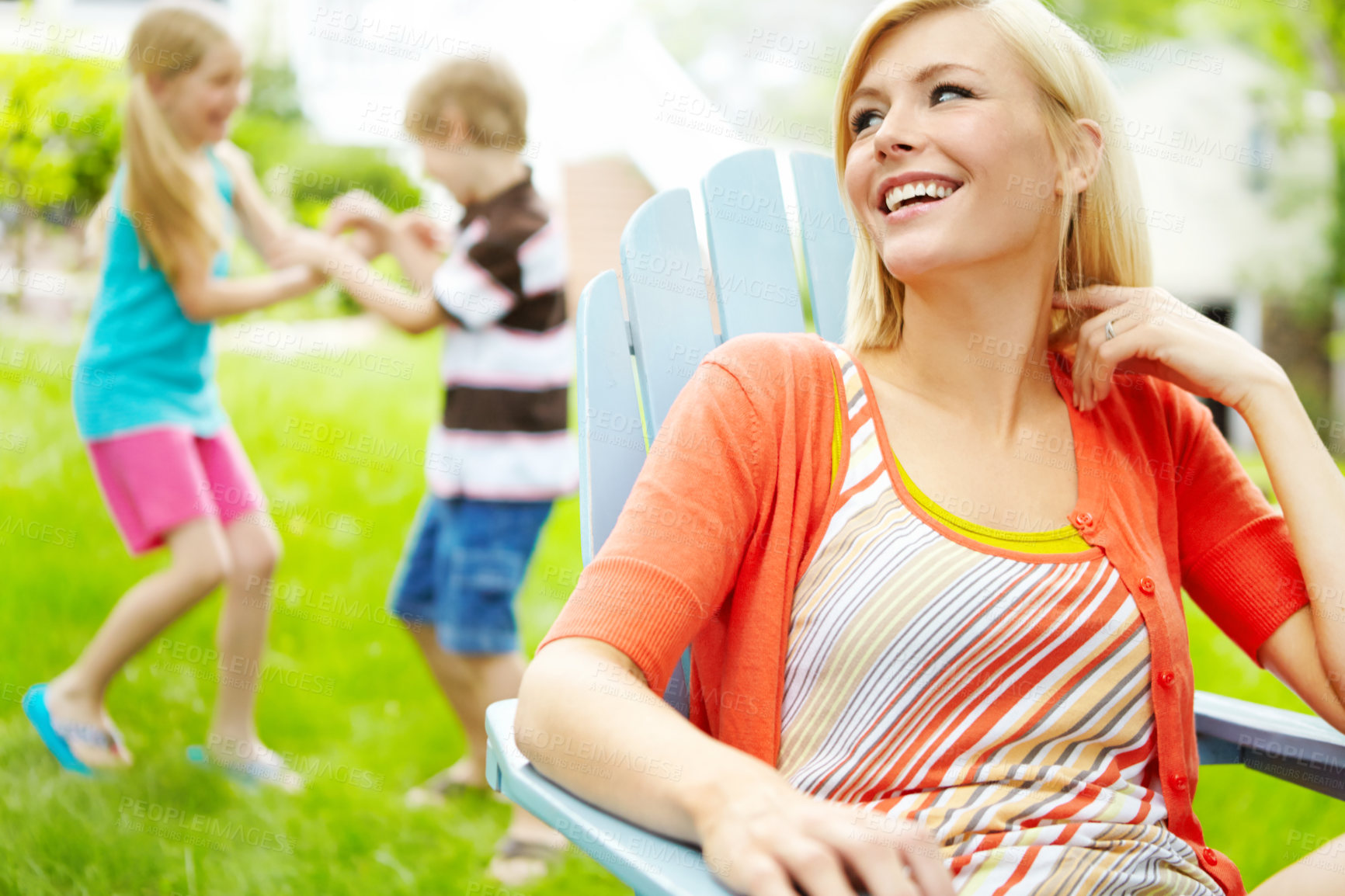 Buy stock photo Happy young mother sitting outdoors as her children play behind her