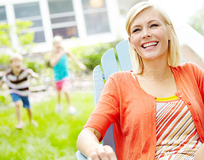 Buy stock photo Summer, portrait and woman with smile, backyard and children with games, house and playing in weekend. Relax, fun and happy with kids, cheerful and comfortable on chair, calm and break for mom