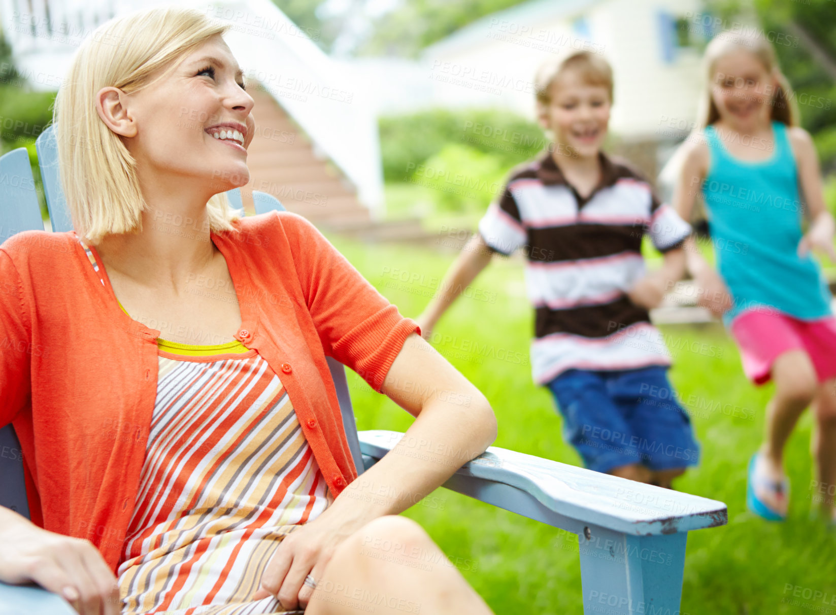 Buy stock photo Happy young mother sitting outdoors as her children play behind her