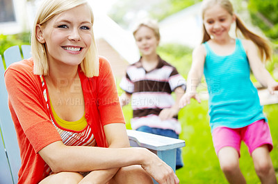 Buy stock photo Happy young mother sitting outdoors as her children play behind her