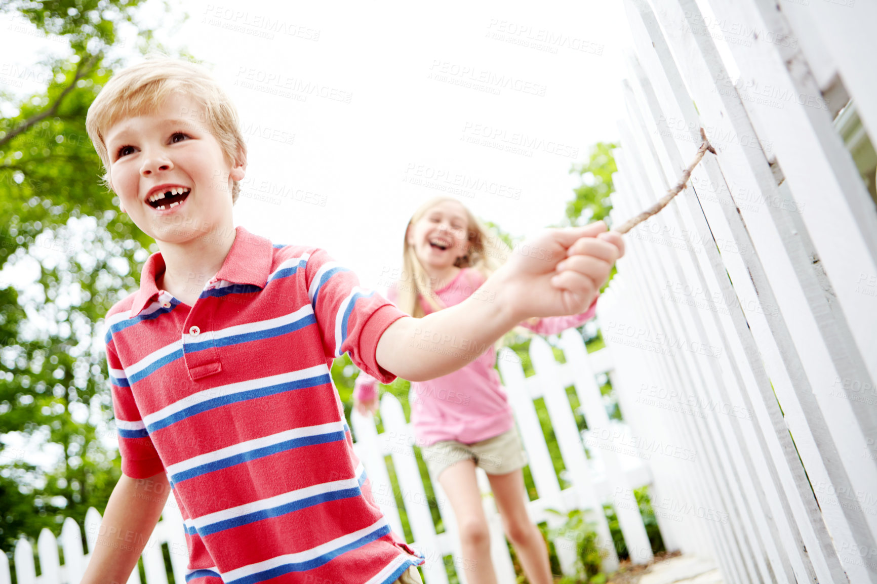 Buy stock photo Happy kids, siblings or running with stick for playful summer together in nature or backyard. Children, brother and sister with smile for fun childhood, bonding or holiday weekend in garden by fence