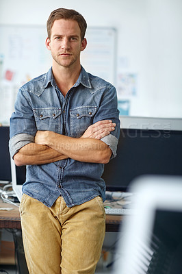 Buy stock photo A young casual businessman leaning against his desk in his office