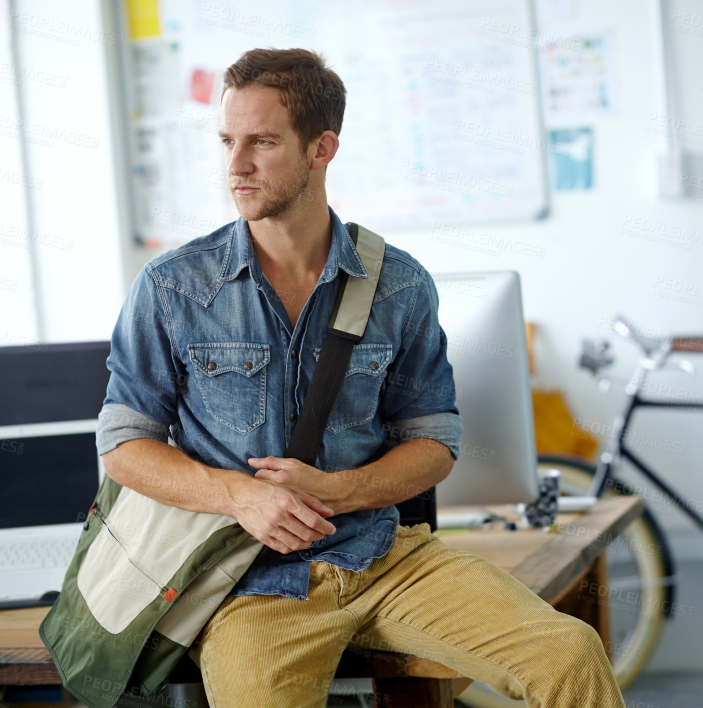 Buy stock photo A young man with a satchel bag sitting on his desk while looking out the window